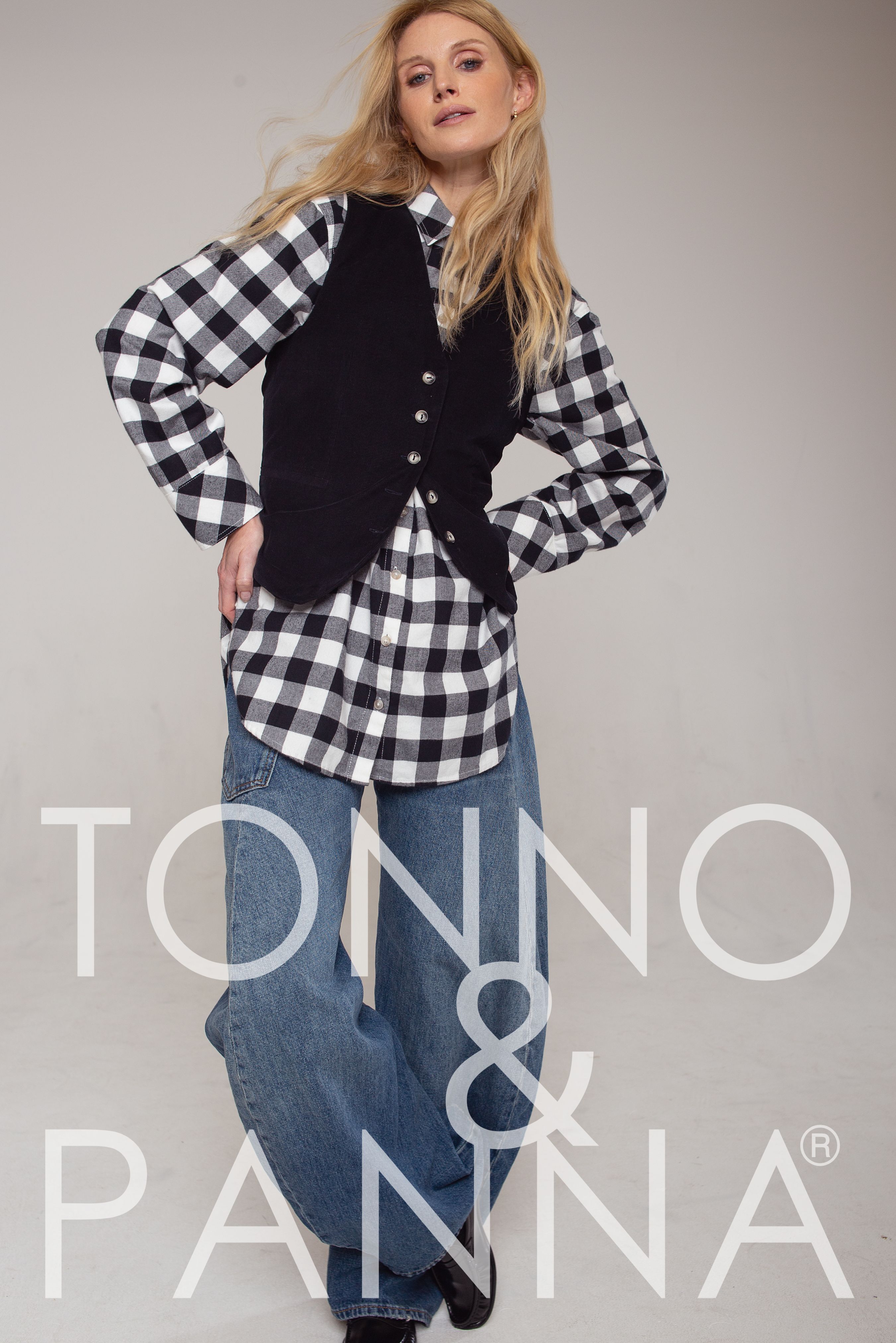 Frau trägt oversized Plaid-Shirt mit schwarzem Weste, weite Jeans, lässig posierend.